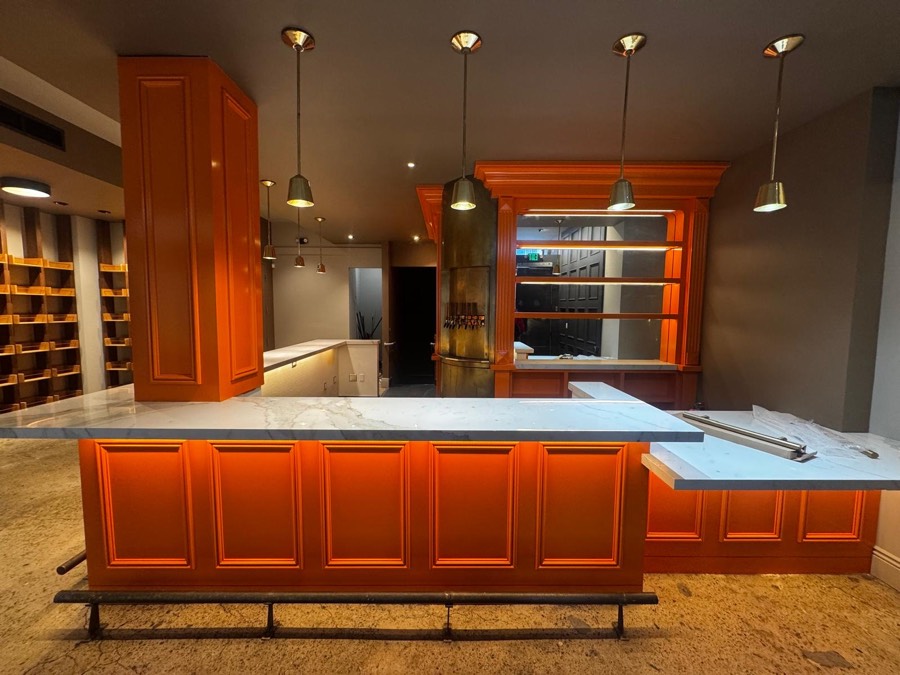 The orange paneled bar seen from the front, with brass lights, the beer taps, and empty shelves waiting to be filled