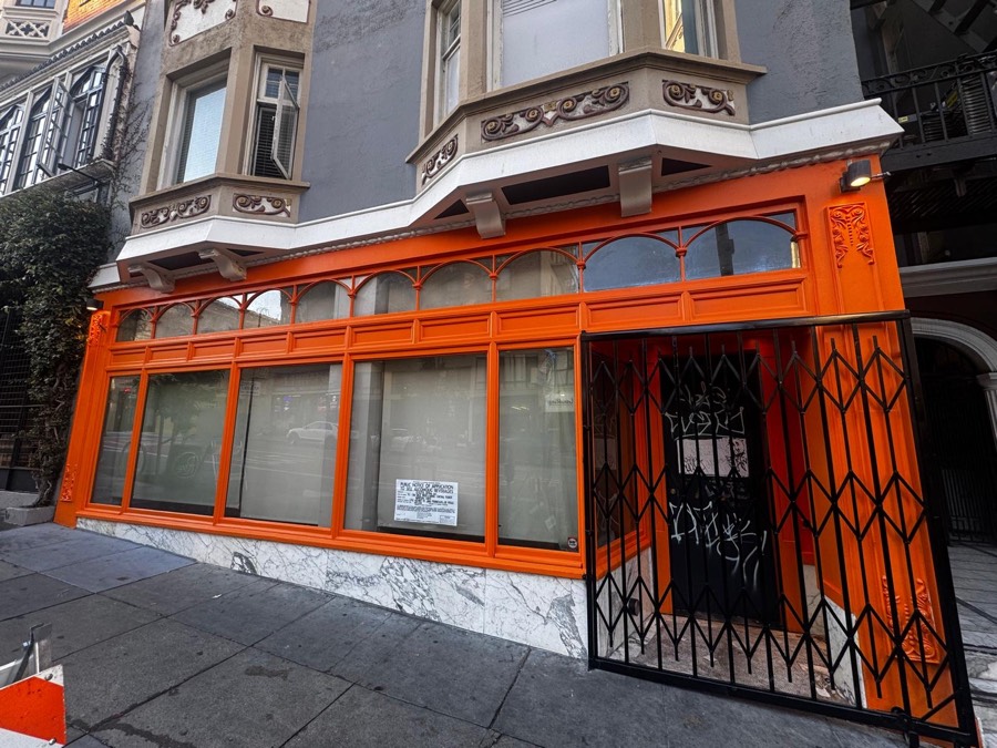 Wanjai's newly painted orange storefront on Geary Street at dusk, lit from inside, with a young tree on the sidewalk