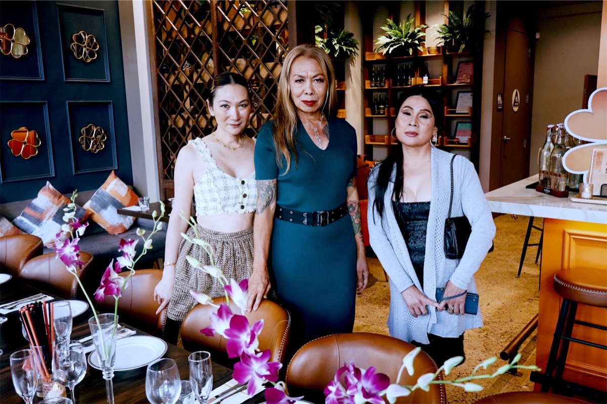 Three guests dressed up for the party, standing by the table set with pink orchids