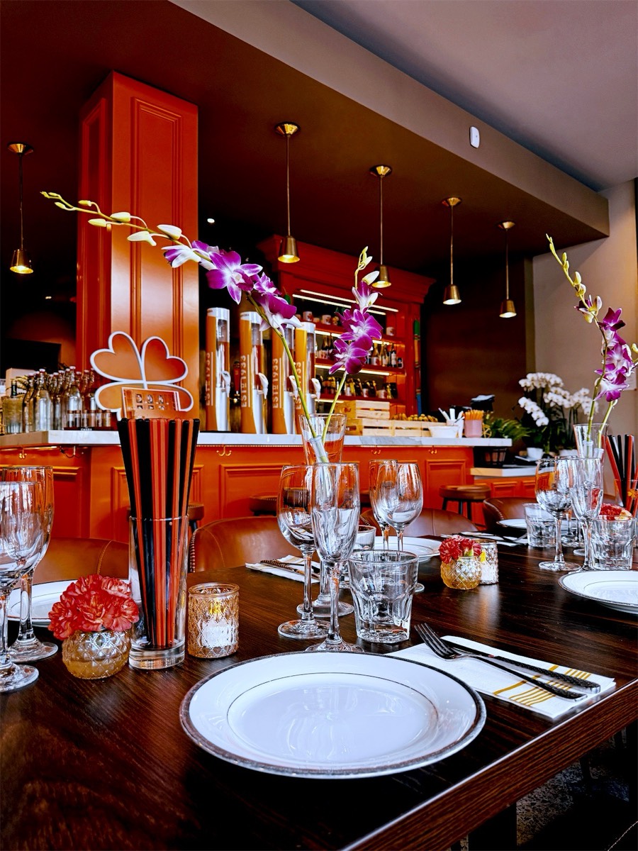 The party table set with white plates, wine glasses and pink orchids, the orange bar behind