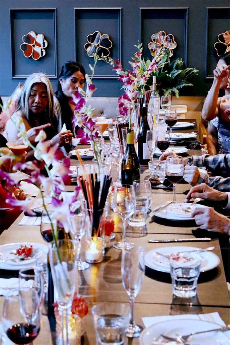 Guests around the table under the clover wall, with wine and shared plates