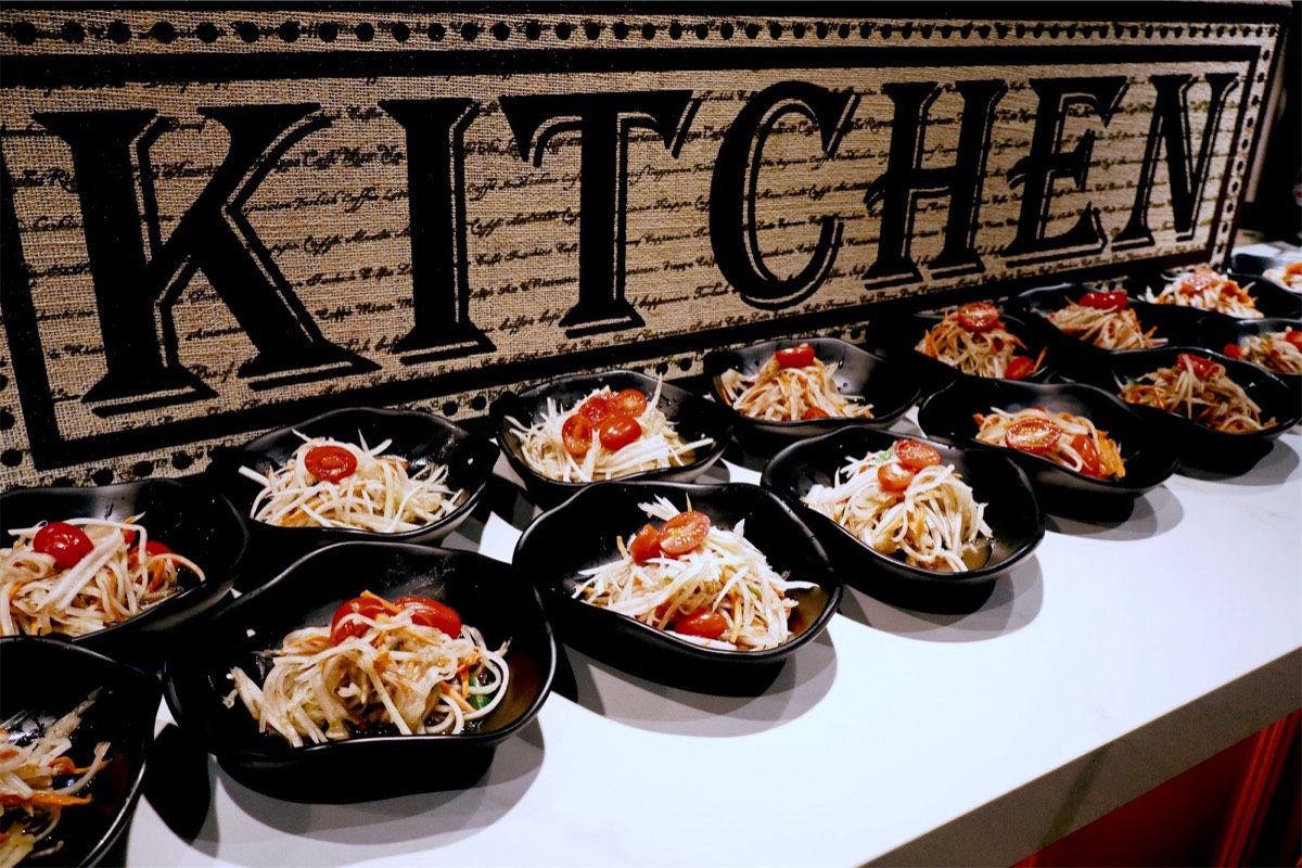 Rows of papaya salad in small black bowls, lined up for the guests