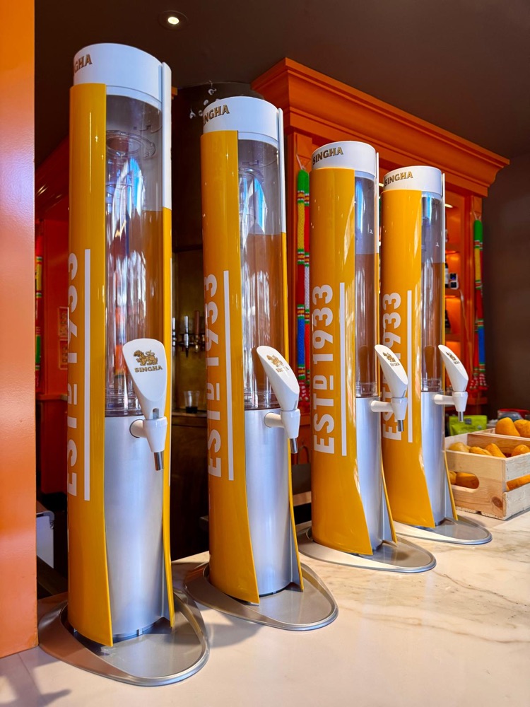 Four yellow Singha beer towers lined up on the marble bar at Wanjai, with the orange shelves behind