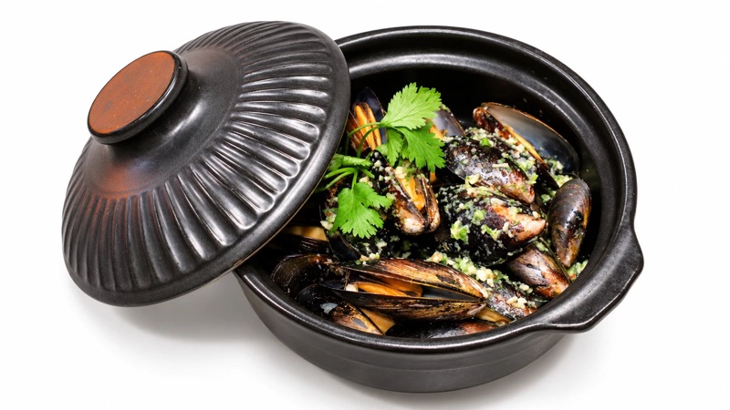 Mussels steamed in a black clay pot with garlic, chili and coriander, the lid set to one side