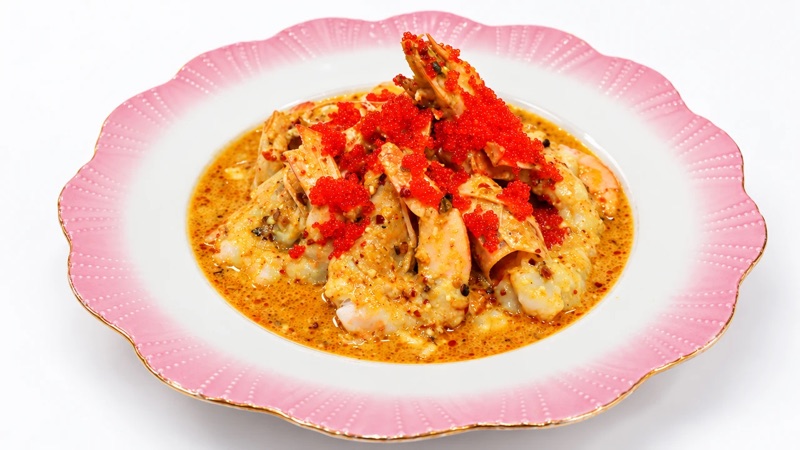Prawns in a chili and garlic sauce under a spoonful of orange roe, on a pink scalloped plate